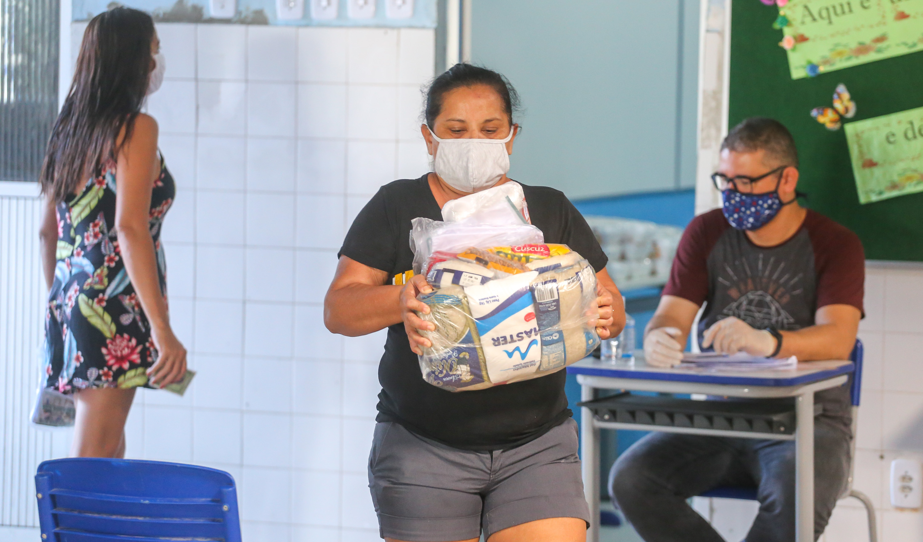 mulher carrega uma cesta básica ao sair de uma sala em uma escola